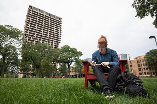 tudent sitting in Adirondack chair near University Hall